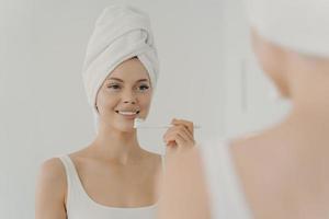 Healthy beautiful woman with towel on head after shower having toothy smile while gently brushing her teeth photo