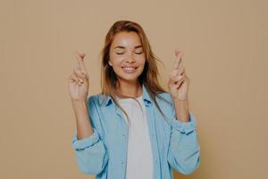 Young woman with crossed fingers on beige background photo
