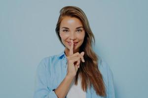 Beautiful woman showing shush gesture on light blue background photo