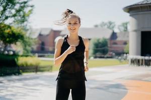 Happy energetic sportswoman runs on stadium has pony tail floating on wind dressed in activewear being active runner has positive smile enjoys regular morning trainings motivates you for sport photo