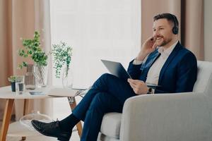 un trabajador profesional alegre que participa en una conferencia en línea usa auriculares de computadora portátil tiene una expresión feliz tiene comunicación a distancia con socios comerciales ve un seminario web. hombre entrenador interior foto