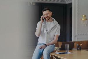 freelancer hablando por teléfono mientras está sentado en el escritorio de trabajo en la oficina de casa foto