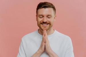 Young happy man with closed eyes praying and asking for something photo