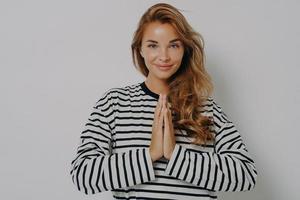 mujer joven positiva sonriente con las manos cruzadas en gesto de namaste y sonriendo a la cámara foto