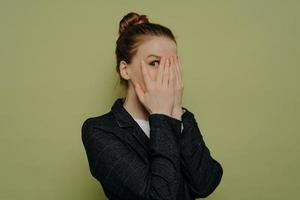 Young woman in formal wear closing face with hands photo