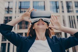 Immersed woman looking up in virtual reality while wearing portable VR, standing on city street photo