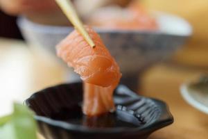 Salmon sashimi in chopsticks dipping with soy sauce photo