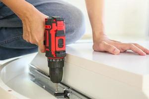 man assembling white table furniture at home using cordless screwdriver photo