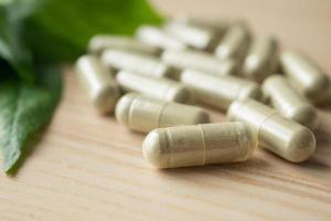 Herbal medicine capsules with Andrographis paniculata leaf on wood table photo