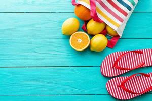Summer fun time and fruits on blue wooden background. Mock up and picturesque. Orange, lemon fruit in bag and flip flops on the floor. Top view and copy space photo
