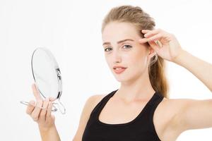 Young caucasian blonde woman looking wrinkles on face in mirror isolated on white background. Skin care and makeup concept. Copy space photo