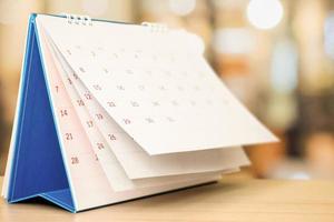 white paper desk calendar on wood table with blurred bokeh background appointment and business meeting concept photo