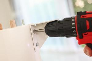 man assembling white table furniture at home using cordless screwdriver photo