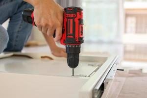 man assembling white table furniture at home using cordless screwdriver photo