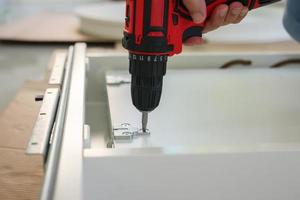 man assembling white table furniture at home using cordless screwdriver photo