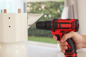 man assembling white table furniture at home using cordless screwdriver photo