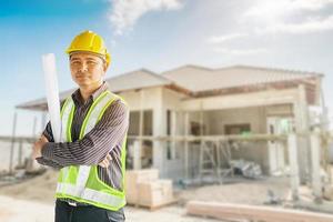 retrato de un hombre de negocios asiático trabajador ingeniero de la construcción en casco protector y papel de planos a mano en el fondo del sitio de construcción de la casa foto