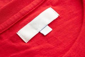 White blank clothing tag label on new red cotton shirt fabric texture background photo