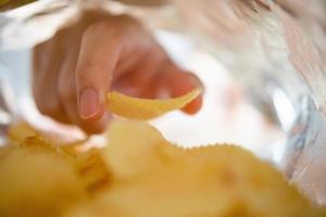 Hand picking potato chips inside snack bag photo