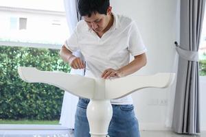 Asian man assembling white table furniture at home photo