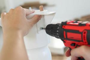 man assembling white table furniture at home using cordless screwdriver photo