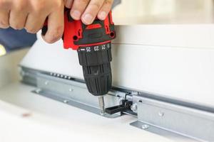 man assembling white table furniture at home using cordless screwdriver photo