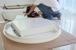 Asian man assembling white table furniture at home photo