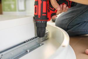 man assembling white table furniture at home using cordless screwdriver photo