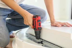 man assembling white table furniture at home using cordless screwdriver photo