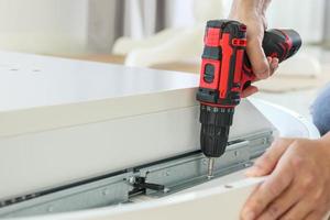 man assembling white table furniture at home using cordless screwdriver photo