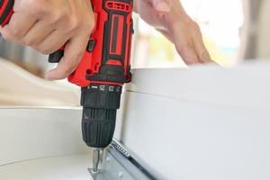 man assembling white table furniture at home using cordless screwdriver photo