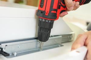 man assembling white table furniture at home using cordless screwdriver photo