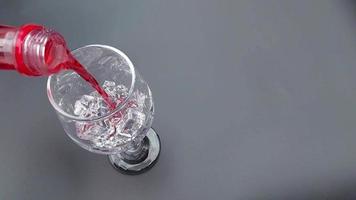 Pour Cola with ice cubes. Cola with Ice and bubbles in the glass. Soda closeup. Pouring red soft drinks into a glass full of ice cubes against a red background. Beverage and drink video