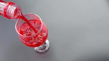 Pour Cola with ice cubes. Cola with Ice and bubbles in the glass. Soda closeup. Pouring red soft drinks into a glass full of ice cubes against a red background. Beverage and drink video