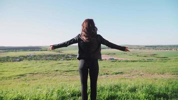 A young woman stands amid the beautiful scenery of green fields and raises his hands up. The joy of victory. Motivational video. Slow motion. Shooting on the Steadicam video