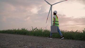 vrouw professioneel ecologie specialist in uniform met speciaal uitrusting in hand- gaat naar onderhoud een windmolen. alternatief en hernieuwbaar energie. modern technologie. groen elektriciteit concept. video