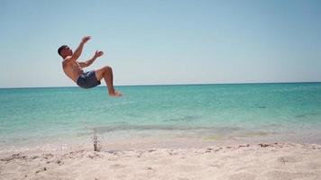 hombre atlético haciendo voltereta hacia atrás en la playa del mar. concepto de vacaciones de verano. camara lenta. video