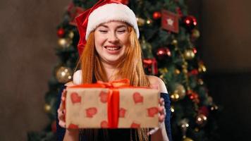 retrato. una hermosa mujer pelirroja con un sombrero de santa felicita a sus familiares por la navidad a través de una videoconferencia. comunicación remota en el nuevo año debido al coronavirus. concepto técnico moderno. video