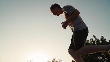 el hombre feliz y juguetón corre y se regocija por el éxito. un joven divertido corriendo y saltando de felicidad contra el telón de fondo de una hermosa puesta de sol. camara lenta video