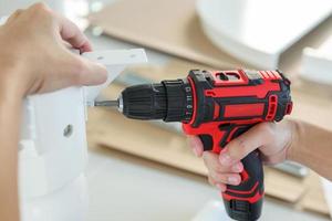 man assembling white table furniture at home using cordless screwdriver photo