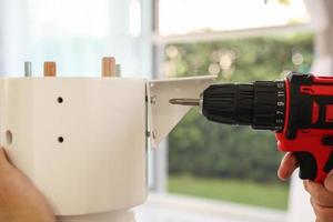 man assembling white table furniture at home using cordless screwdriver photo