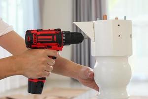 man assembling white table furniture at home using cordless screwdriver photo