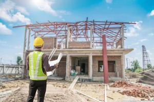 young professional engineer in protective helmet and blueprints paper at the house building construction site photo