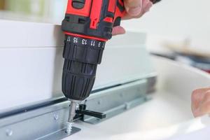 man assembling white table furniture at home using cordless screwdriver photo