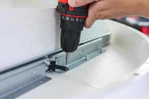 man assembling white table furniture at home using cordless screwdriver photo