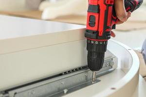 man assembling white table furniture at home using cordless screwdriver photo