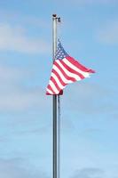 An old American flag on the tip of the flag with a torn in the wind on the flagpole against a blue sky background. photo