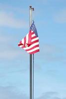 An old American flag on the tip of the flag with a torn in the wind on the flagpole against a blue sky background. photo