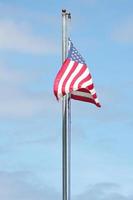 An old American flag on the tip of the flag with a torn in the wind on the flagpole against a blue sky background. photo