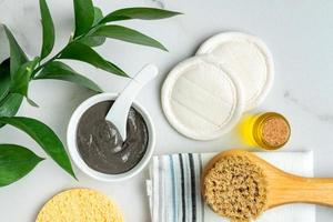 Top view of home spa accessories - reusable sponges, natural oil, brush for dry massaging, clay mask and cotton towel on wooden background. photo